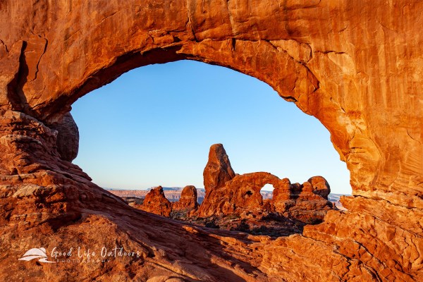 Turret Arch glows orange as seen through North Window just after sunrise in Utah's Arches National Park.